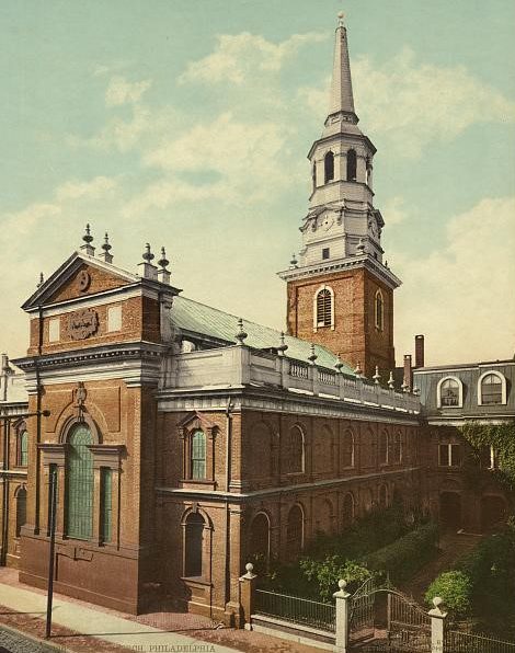 A colorized photograph of Christ Church taken in 1901. A prominent georgian church dominates the photograph, with a gated green courtyard to the right of the main church building.