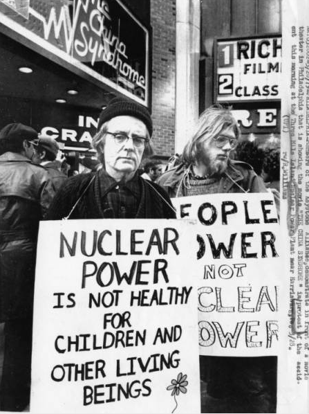 A black and white photograph of protesters holding signs in front of a movie theater. The theater marquee is advertising the film The China Syndrome. Signs read