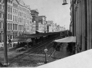 A black and white photograph of sheds running down the median in Market Street. Streetcar tracks are visible on either side. 