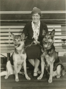 a black and white photograph of a woman flanked by two German Shepherd Dogs