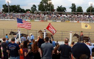 Cowtown Rodeo ring with audience in foreground and background and flag bearing horse riders in between.