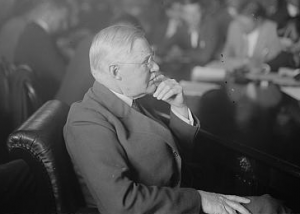 This black and white photograph shows Joseph R. Grundy in a board meeting. The other board members are in the background while the camera focuses on Grundy.