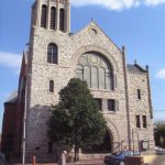 This color photograph shows the Mother Bethel AME Church. A large stained glass window appears near the top and the outer later is comprised of layered stone.