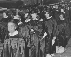 This black and white photograph shows a group of students in graduation gowns lined up on a Philadelphia street.