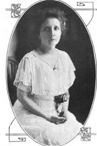 a black and white portrait of Mabel Lloyd Ridgely, seated in a white lace dress. A rolled up poster or magazine is tucked under her arm.