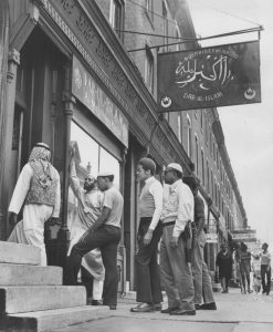 Black and white photograph depicting five muslim men in different styles of Muslim dress entering a mosque.