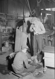 Black and white photograph depicting two men blowing glass.