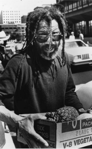 A black and white photograph of John Africa carrying a cardboard box of fruit