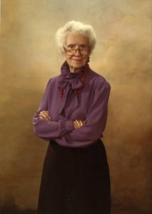 Color portrait of Maggie Kuhn. She is wearing a purple blouse, black skirt, and a red necklace.