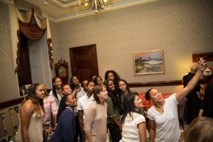 Color photograph depicting Dawn Staley holding a cellphone to take a selfie with Governor Nikki Haley and her team of women basketball players.