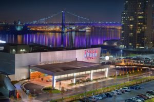 Color photograph showing the SugarHouse Casino with the Benjamin Franklin Bridge in the background.