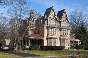 a color photograph of a the twin "Centennial House" built in an eclectic Gothic Revival style. The home features tall peaked roofs, wide porches, and two-story bay windows.