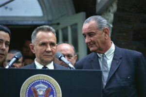 A color photograph of Lyndon B. Johnson and Alexi Kosygin standing at a podium with microphones. The Seal of the President of the United States of America is displayed on the front of the podium.