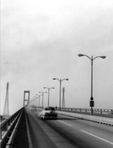 A black and white photograph of cars driving over the Delaware Memorial Bridge.