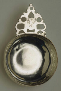 A color photograph of a silver bowl with an ornate handle on one side.