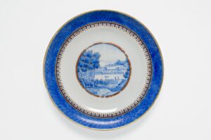 Blue rimmed white china plate with interior image of river and building