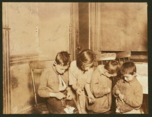 A group of children sit together stringing tags for work.