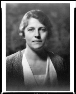 A black and white photograph of Pearl Buck as a young woman. She is dressed in a silk blouse and sweater and faces the camera.