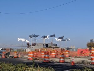 Photograph depicts an outdoor art installation showing fish-like scultpures suspended by rods in the air.