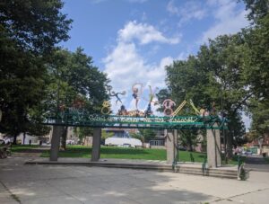 Image depicts a colorful gate with sculptures of performers dancing along the top.