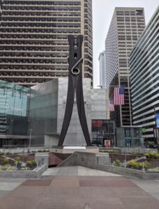 Photograph shows a large silver metal sculpture of a clothespin.