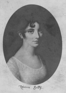 A black-and-white portrait of a young Rebecca Gratz. Her dark hair is pulled back with a singular curl draping over her forehead. She wears a lightly dotted blouse or dress.