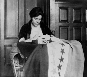 Photograph of Alice Paul sewing a star onto a flag.